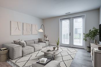 A modern living room with a grey sofa, a coffee table, and a large window with blinds.