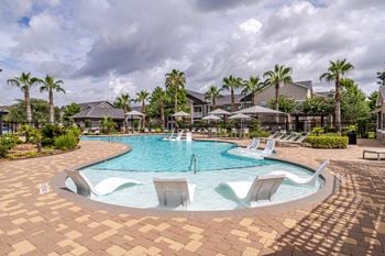 A pool surrounded by palm trees and lounge chairs.