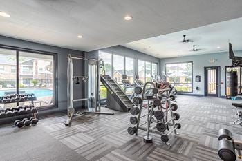 A spacious gym with a variety of equipment and a view of a pool and houses outside the windows.