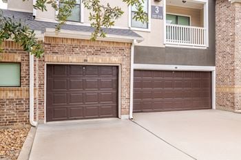 Two brown garage doors in front of a brick building.