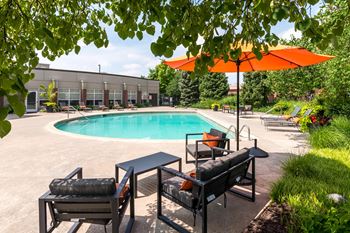 A pool area with a table and chairs and an orange umbrella.