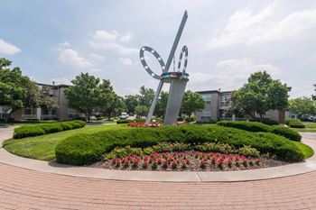A large sculpture in the shape of a heart is surrounded by a circular garden with red flowers.