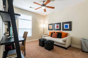 A living room with a white couch, a black ottoman, a ceiling fan, and three framed pictures on the wall.
