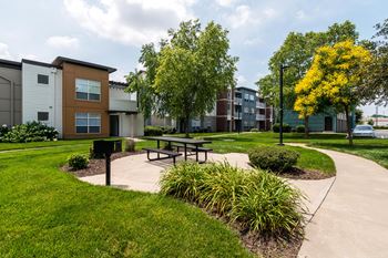 A park area with a picnic table and benches in front of apartment buildings.