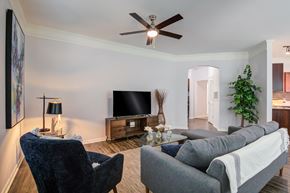Overland Park apartment for rent - A living room with a grey couch, a blue chair, a television, and a ceiling fan at Sovereign at Overland Park Apartments, Overland Park, KS