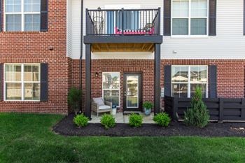 A balcony with a black railing and a pink chair is on the second floor of a brick building.