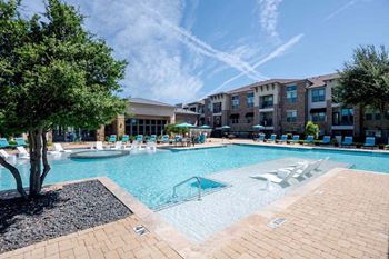 A large swimming pool with lounge chairs in front of a building