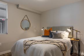 Vancouver apartment for rent - 1-Bedroom Apartments in Vancouver, WA - 134th Street Lofts - Bedroom with Cream Walls, Bed, Nightstands with Lamps, Round Wall-Mounted Mirror, and Window.