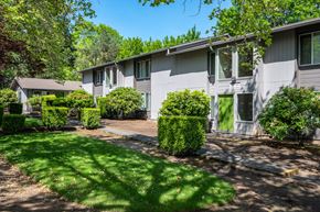 Tigard apartment for rent - the front of a white house with green trees and bushes