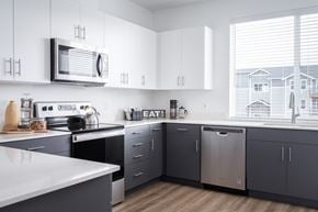Oregon City townhouse for rent - 2 BR Apartments in Oregon City OR - Timberview Apartments and Townhomes - Bright Modern Kitchen with a Large Window, Stainless Steel Appliances, White Quartz Countertops, and White and Dark Grey Cabinetry