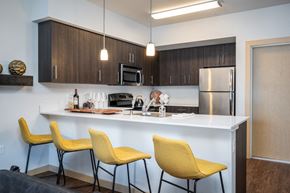 Everett apartment for rent - Dog-Friendly Apartments in Everett WA - The Waterline - Kitchen with Stainless Steel Appliances, Quartz Countertops, Dark Wood-Style Cabinetry, Pendant Lighting, Breakfast Bar, and Vinyl Hardwood Floo