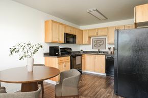 Battle Ground apartment for rent - A kitchen with a black refrigerator, wooden cabinets, and a table with chairs.