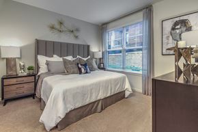 Raleigh apartment for rent - A bedroom with a large bed and a nightstand with a plant on it at Crabtree Lakeside Apartments, Raleigh, NC, 27612