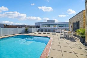 Washington apartment for rent - A swimming pool with a red brick border and a patio area with chairs and a table.