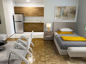 Washington apartment for rent - A modern bedroom with a bed, chair, and a refrigerator.