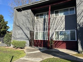 Stockton apartment for rent - A grey and red building with a red awning and a small tree in front.