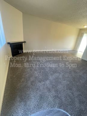 Stockton triplex for rent - A room with a grey floor and a white wall with a black shelf on it.