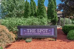 Lansing townhouse for rent - A sign for The Spot Fitness Center + Lounge is displayed in front of some trees.