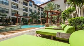 Houston apartment for rent - a large swimming pool with green lounge chairs in front of a building