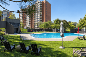Ottawa apartment for rent - A pool surrounded by lawn chairs and umbrellas with a tall building in the background.