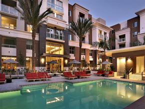 San Diego apartment for rent - A large swimming pool is surrounded by red chairs and palm trees in front of a building. at West Park Apartments, San Diego, CA, 92108