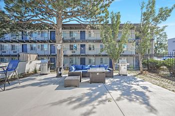 A patio with furniture and trees in front of a building