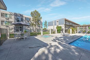 A poolside area with a table and chairs and a building in the background.