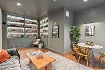 New Haven apartment for rent - A living room with a grey couch, a wooden coffee table, a round table with chairs, and a bookshelf filled with books.