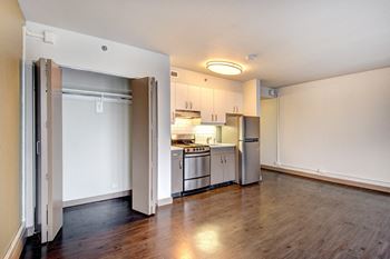 An empty living room and kitchen with a wood floor and white cabinets