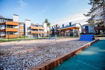 A playground with a blue slide and a pebble-covered area in front of apartment buildings.