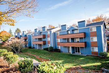 Apartment complex with blue and brown buildings surrounded by trees and grassy areas.