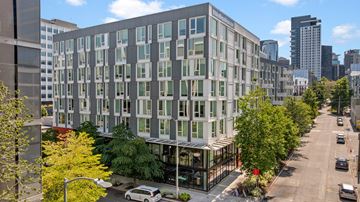 Seattle apartment for rent - A modern building with a glass facade is surrounded by trees and other buildings.