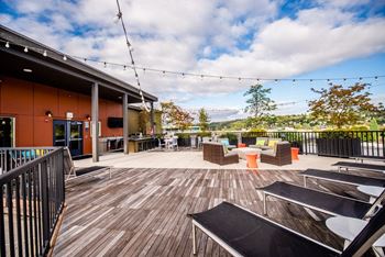 A wooden deck with a black railing and a few chairs and tables.