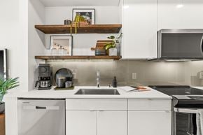 Seattle apartment for rent - A modern kitchen with white cabinets and a wooden shelf above the sink.