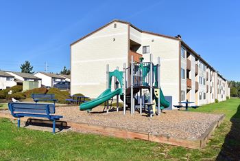 A playground with a green slide and a blue bench in front of a building.