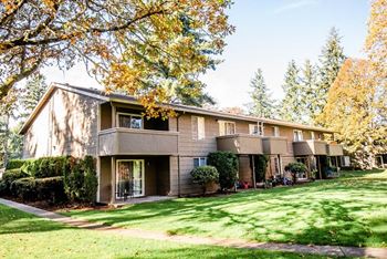 The view of an apartment building with a lawn and trees