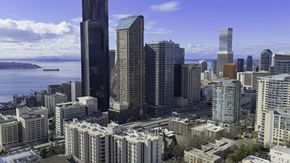 Seattle apartment for rent - A cityscape with a mix of modern and older buildings, a body of water in the background, and a partly cloudy sky.