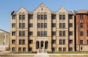 Detroit apartment for rent - A large, beige, multi-story building with a balcony and arched doorways.