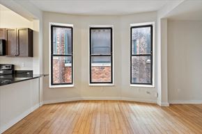 Detroit apartment for rent - an empty living room with three windows and a kitchen in the background