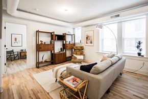 Detroit apartment for rent - A living room with a grey couch, a wooden coffee table, and a large window.