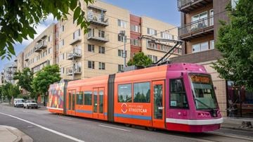 Portland apartment for rent - A streetcar with a pink and orange design is on a street.