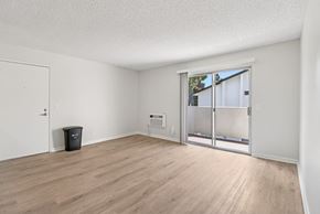 Vista apartment for rent - A room with a white door, a window with a view of trees outside, and a black trash bin on the floor.