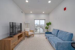 Philadelphia apartment for rent - A living room with a blue couch, a wooden entertainment center, and a window with a view of a balcony.