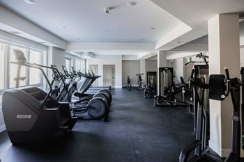 A gym with a row of treadmills and elliptical machines