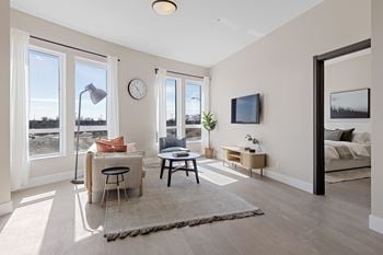 A living room with a sofa, a table, a lamp, a clock, a tv, and a window overlooking a field