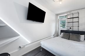 Ottawa apartment for rent - A bedroom with a bed, a chair, and a television mounted on the wall.