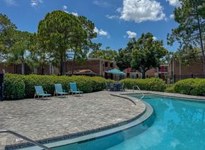 Tampa apartment for rent - A swimming pool surrounded by a brick patio and lawn chairs.