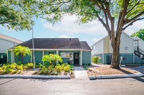 Tampa apartment for rent - A small building with a green roof is surrounded by trees and plants.