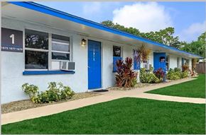 Sarasota apartment for rent - A white building with blue doors and windows has a sign on the left side.