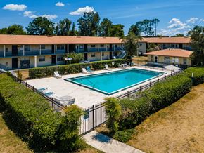 Eustis apartment for rent - A swimming pool surrounded by a fence and bushes in front of a building.